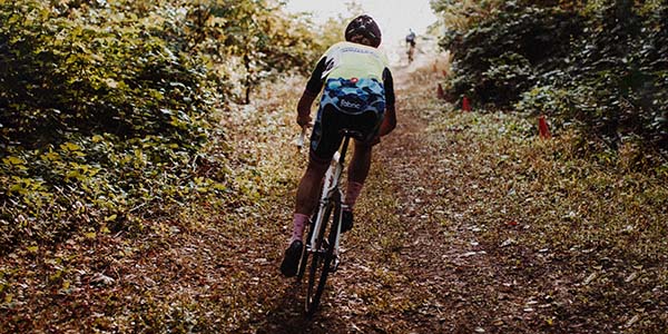 Man riding bicycle away from the viewer on a forest trail.